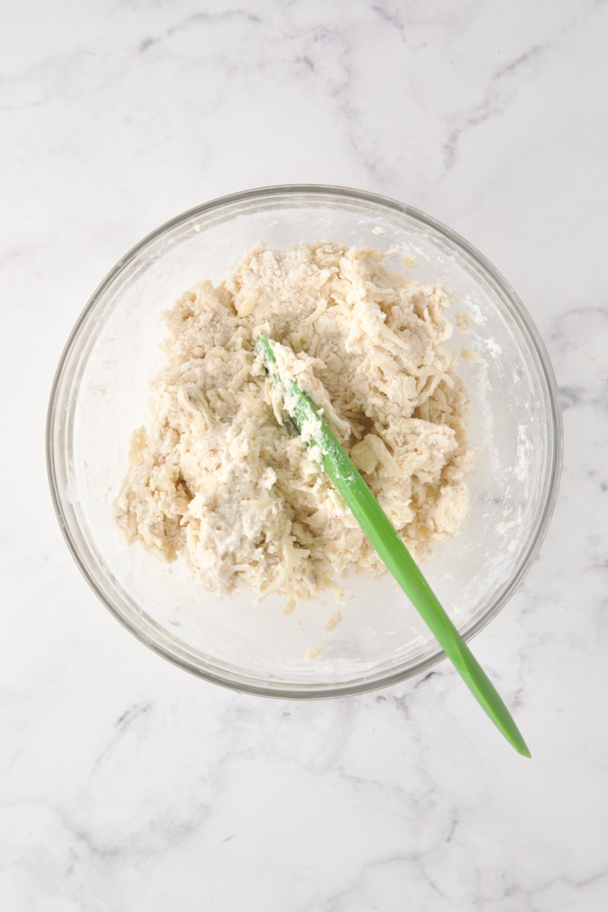 Buttermilk added to biscuit ingredients in glass bowl being stirred with green spatula.