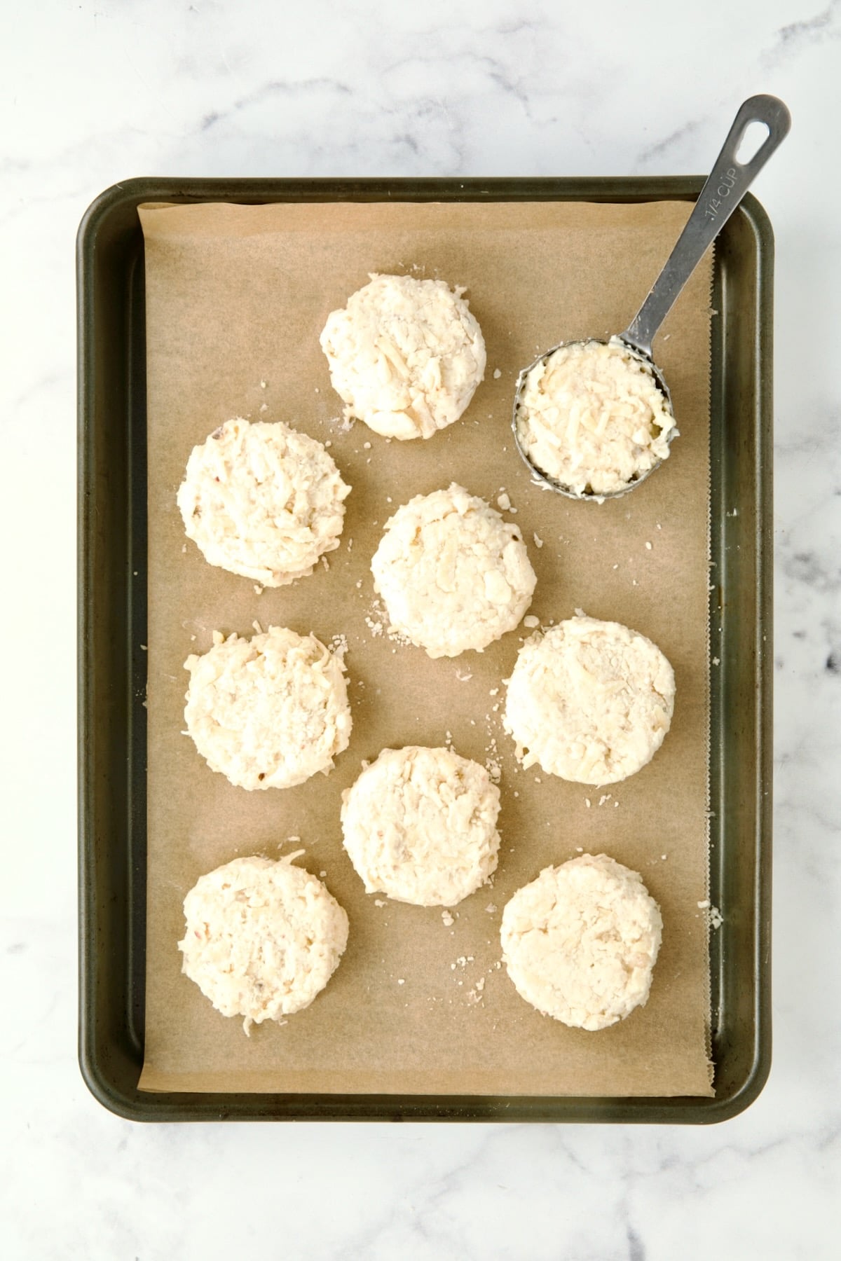 Biscuit batter portioned out into nine biscuits on parchment paper lined rimmed baking sheet.