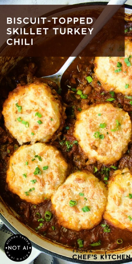 Pinterest graphic for Biscuit-Topped Turkey Skillet Chili showing it in a white enamel cast iron skillet with serving spoon.