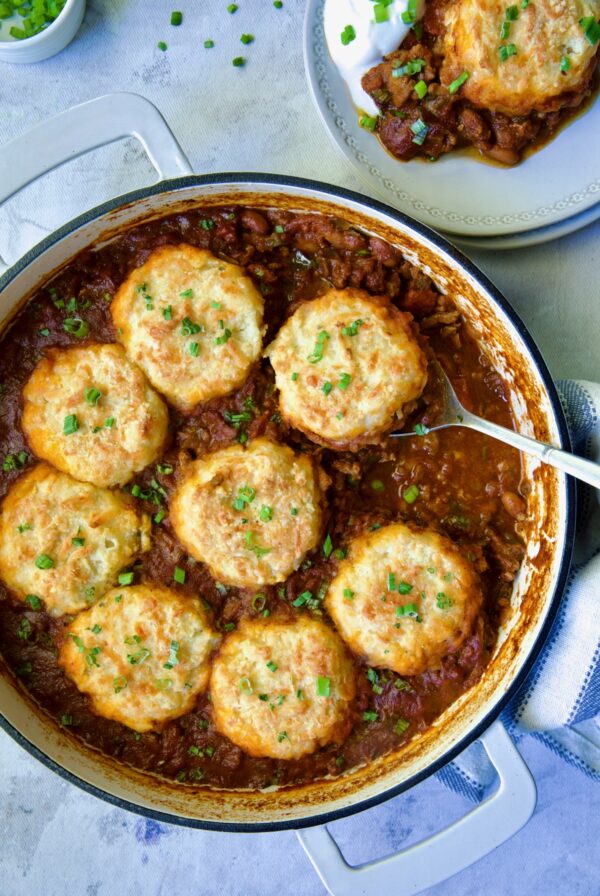 Biscuit-Topped Turkey Skillet Chili in white enamel cast iron skillet with a piece removed onto a small plate.