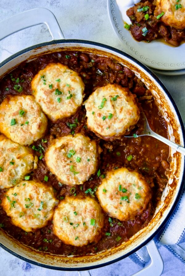 Biscuit-Topped Turkey Skillet Chili in white enamel cast iron skillet with a piece removed onto a small plate.
