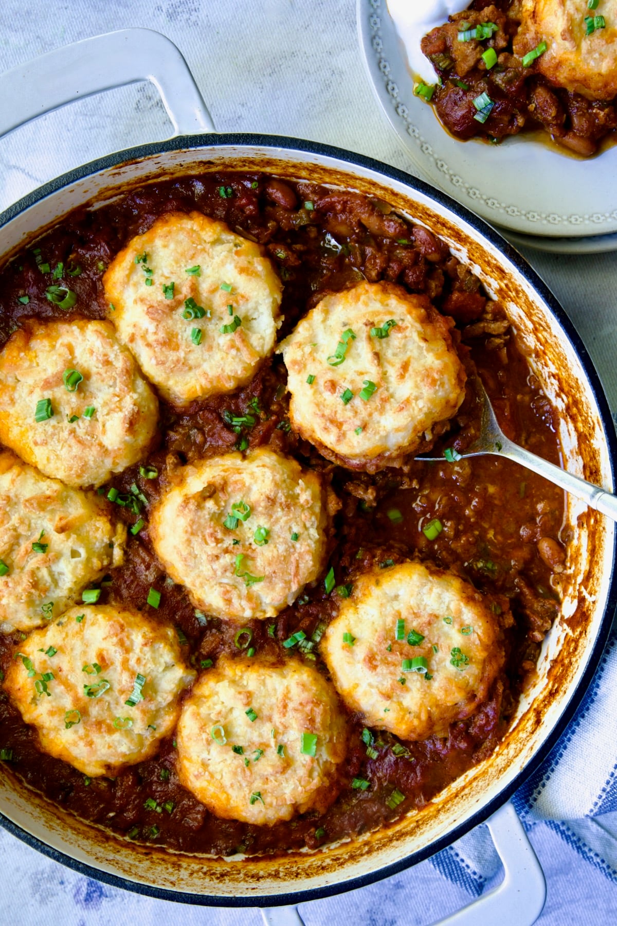 Biscuit-Topped Turkey Skillet Chili in white enamel cast iron skillet with a piece removed onto a small plate.