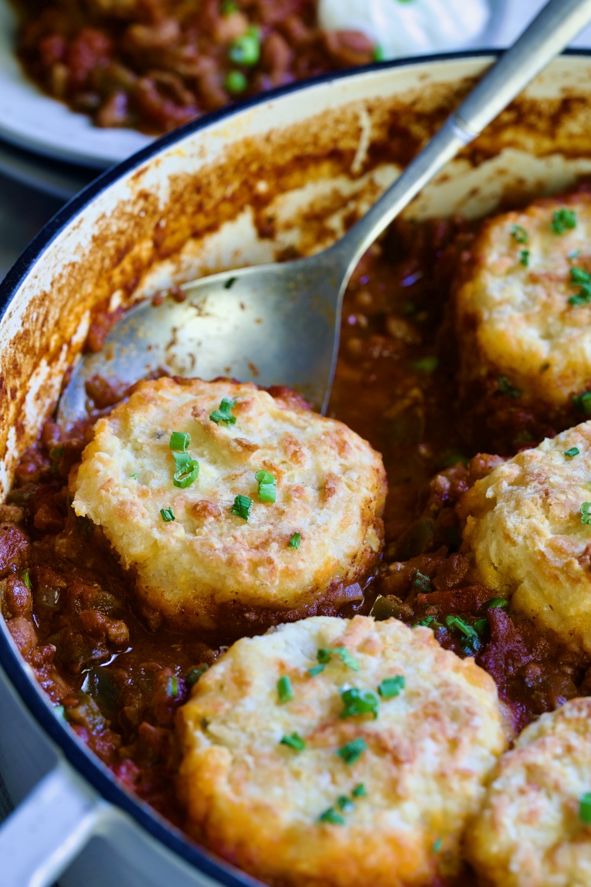 Biscuit-Topped Turkey Skillet Chili in white enamel cast iron skillet with a piece removed with stainless steel spoon.