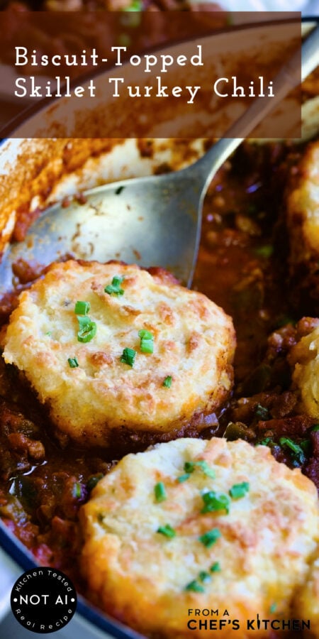 Pinterest graphic for Biscuit-Topped Turkey Skillet Chili showing it in a white enamel cast iron skillet with serving spoon.