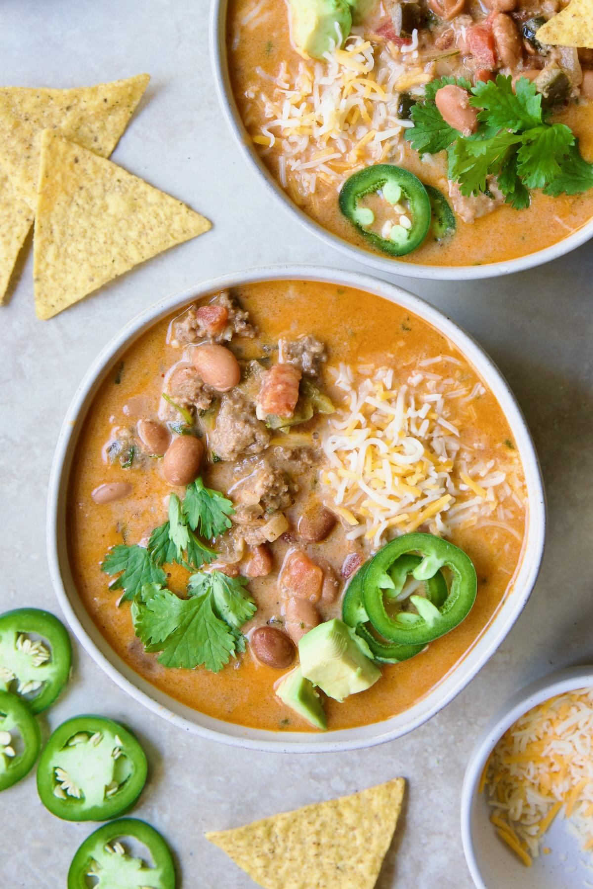 One serving of Creamy Taco Soup in white bowl garnished with tortilla chips, avocado, cheese and jalapeno slices.