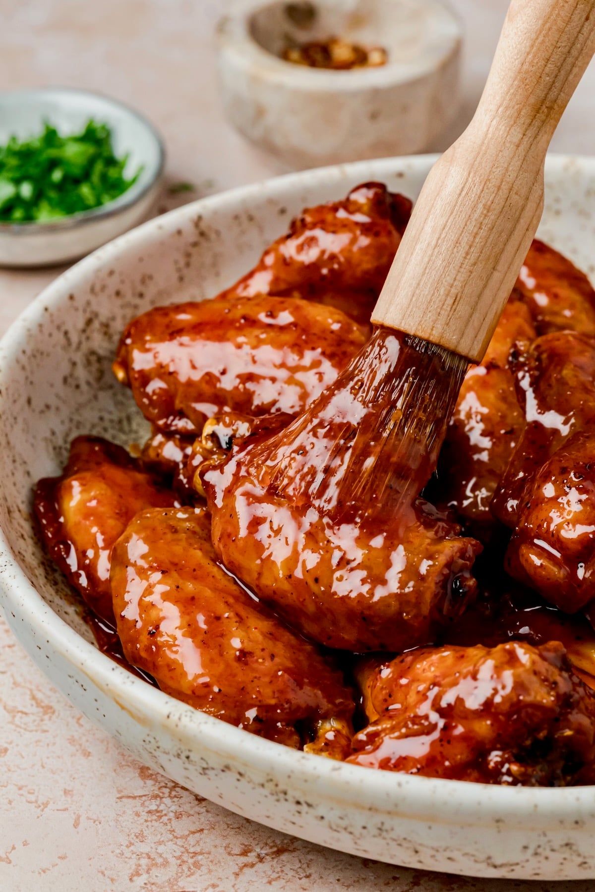 Hot Honey Chicken Wings in speckled bowl being brushed with glass with basting brush.