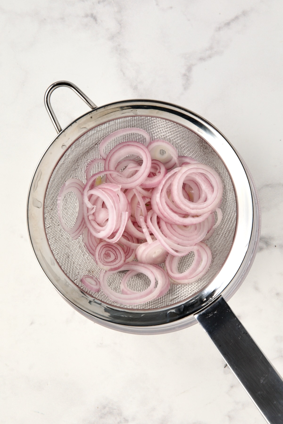 Shallot rings in stainless steel sieve.