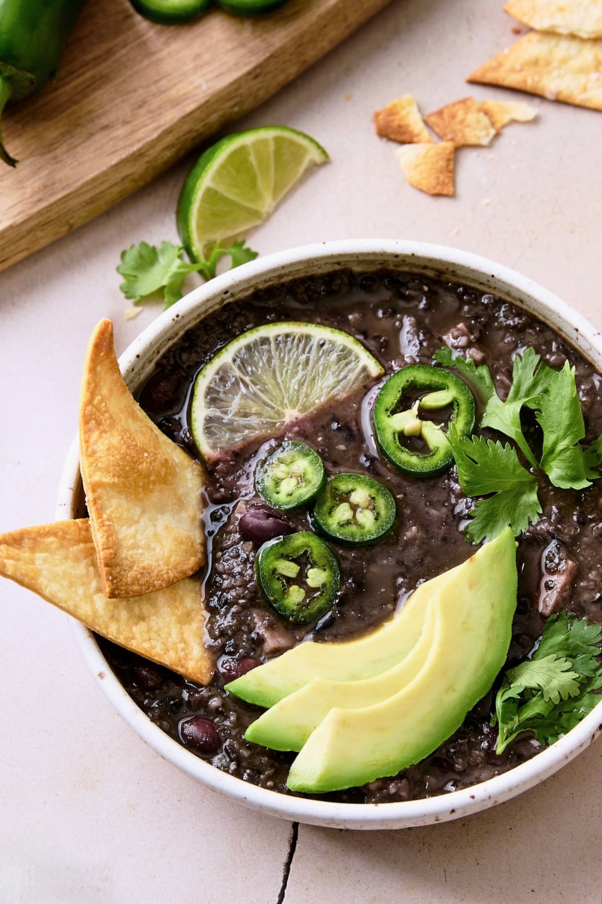 Slow Cooker Black Bean Soup in white bowl garnished with chips, jalapeno slices, lime wedge and cilantro.