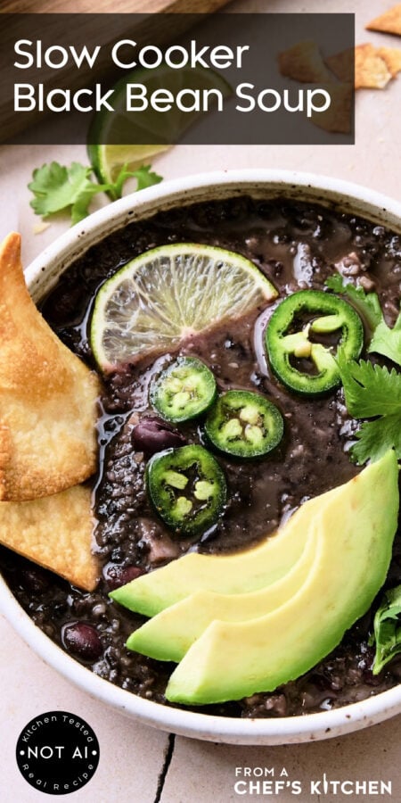 Pinterest graphic for Slow Cooker Black Bean Soup showing it in a white bowl garnished with lime wedges, jalapeno slices, cilantro and avocado.