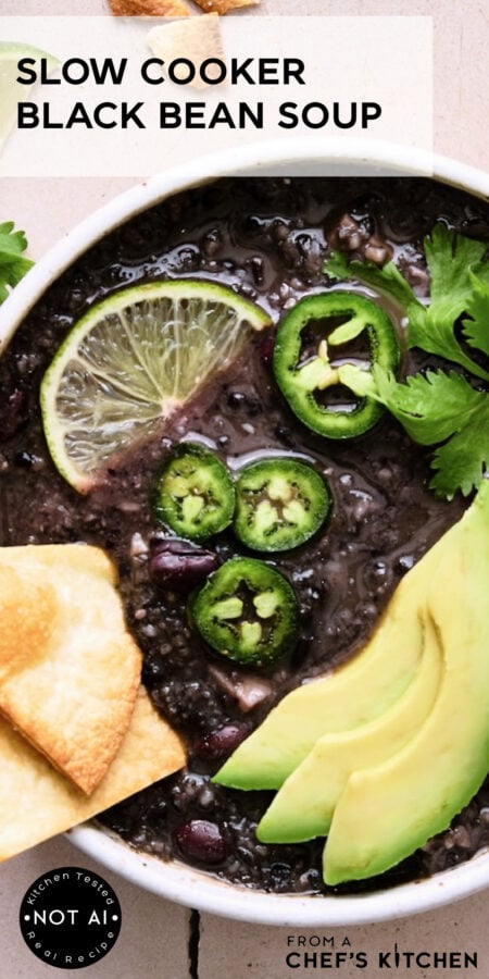 Pinterest graphic for Slow Cooker Black Bean Soup showing it in a white bowl garnished with lime wedges, jalapeno slices, cilantro and avocado.