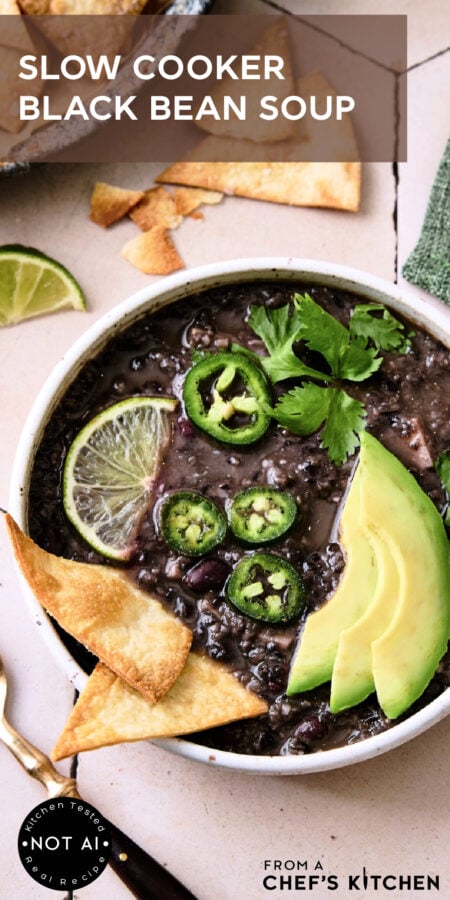 Pinterest graphic for Slow Cooker Black Bean Soup showing it in a white bowl garnished with lime wedges, jalapeno slices, cilantro and avocado.