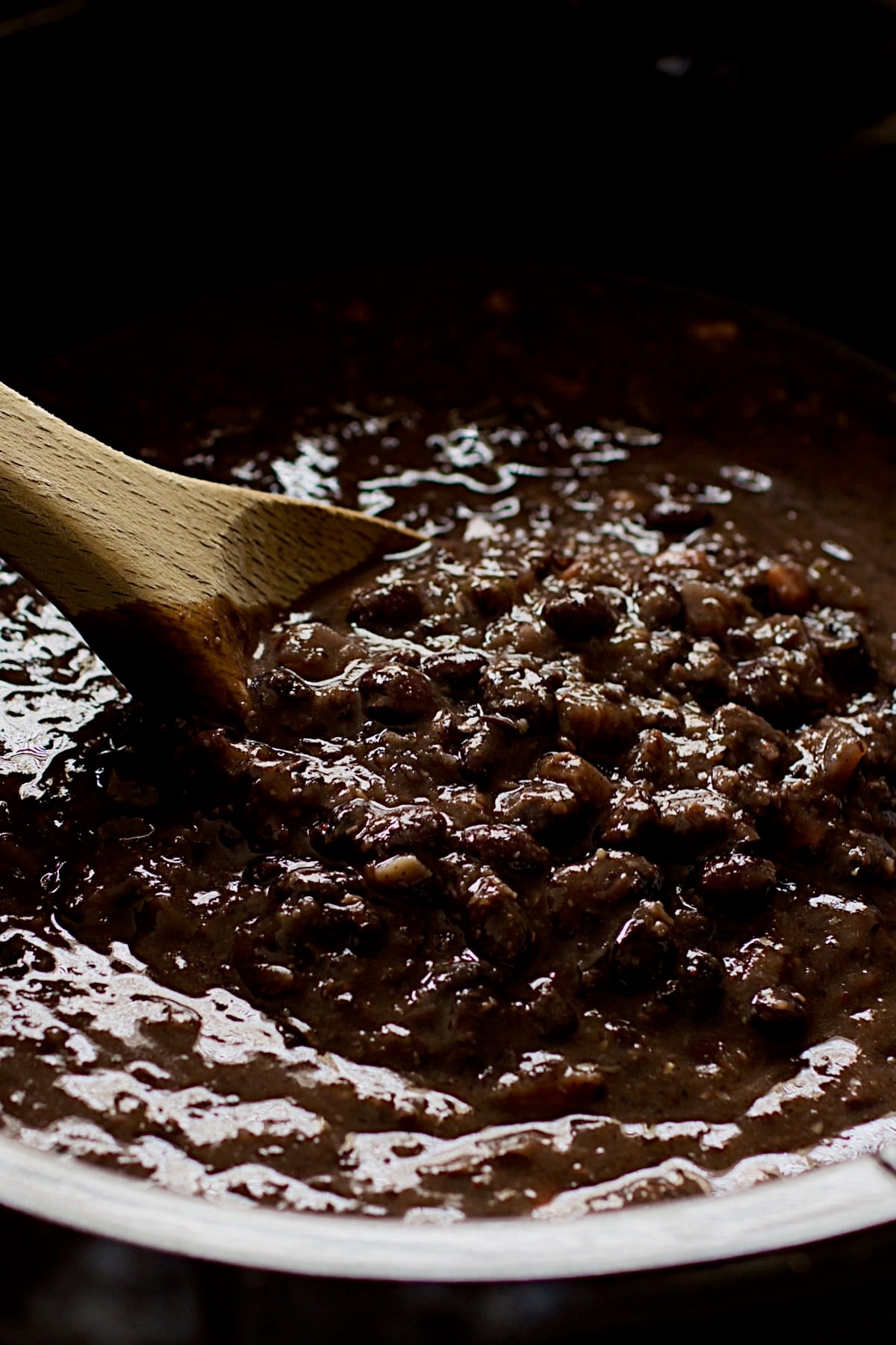 Wooden spoon stirring black bean soup in slow cooker.