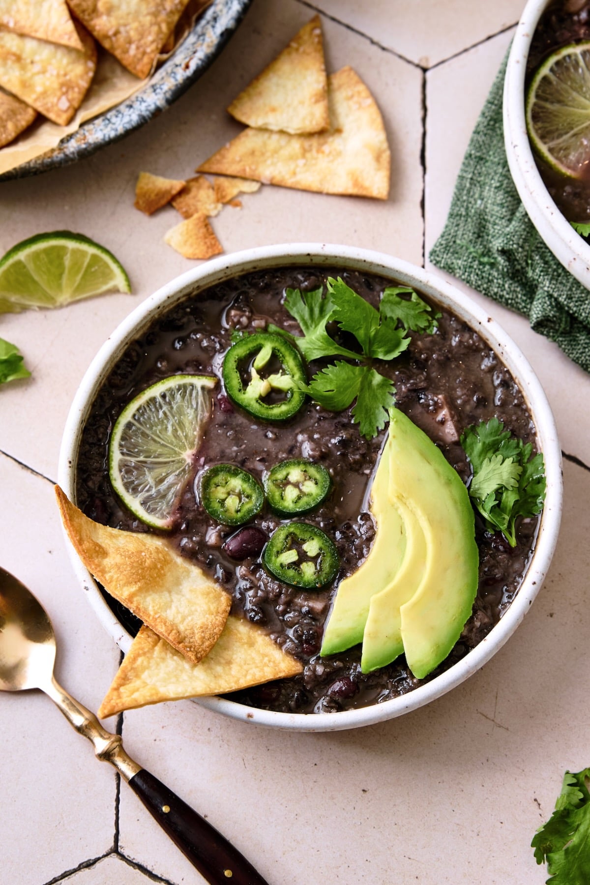 Slow Cooker Black Bean Soup in white bowl garnished with chips, jalapeno slices, lime wedge and cilantro.