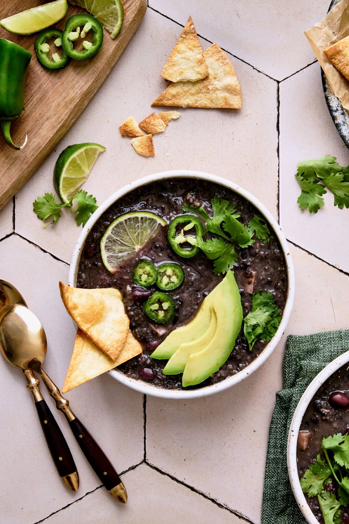 Slow Cooker Black Bean Soup in white bowl garnished with chips, jalapeno slices, lime wedge and cilantro.