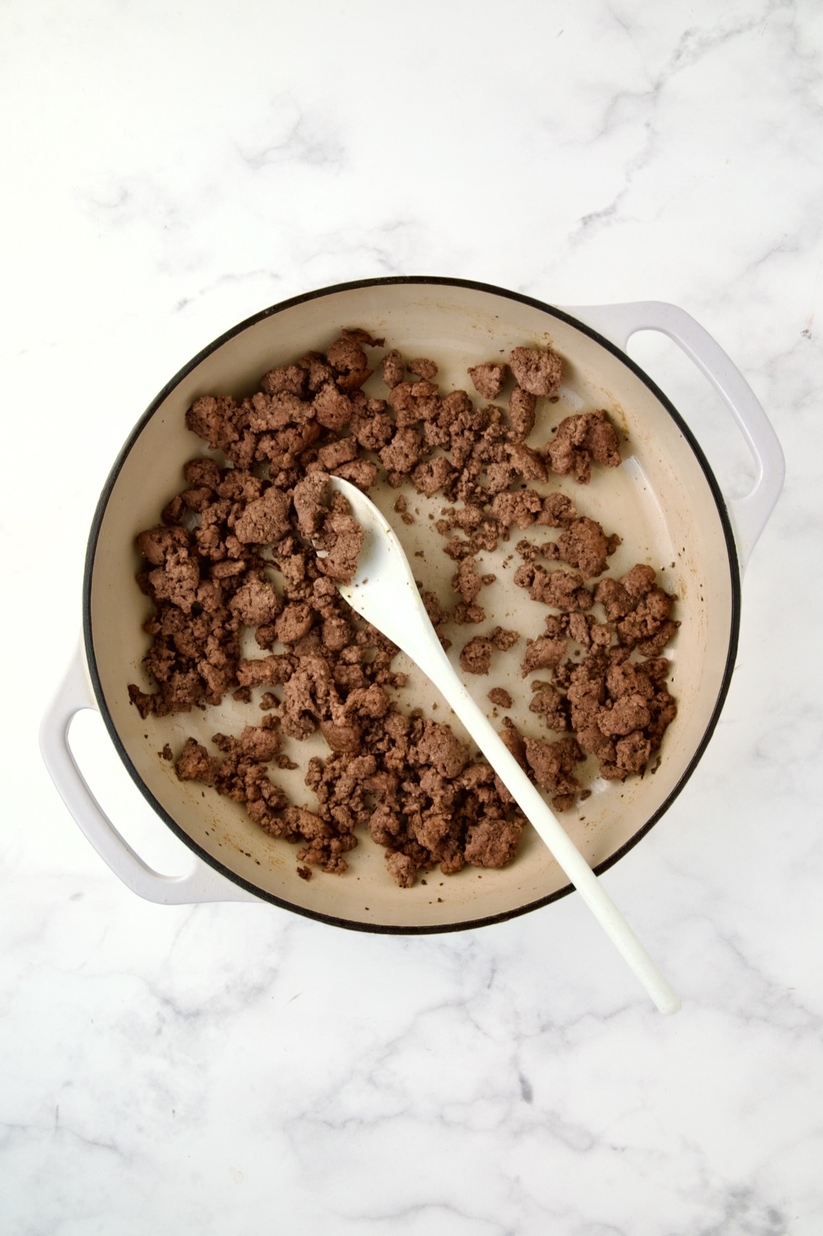 Browned ground beef in white enamel cast iron skillet.