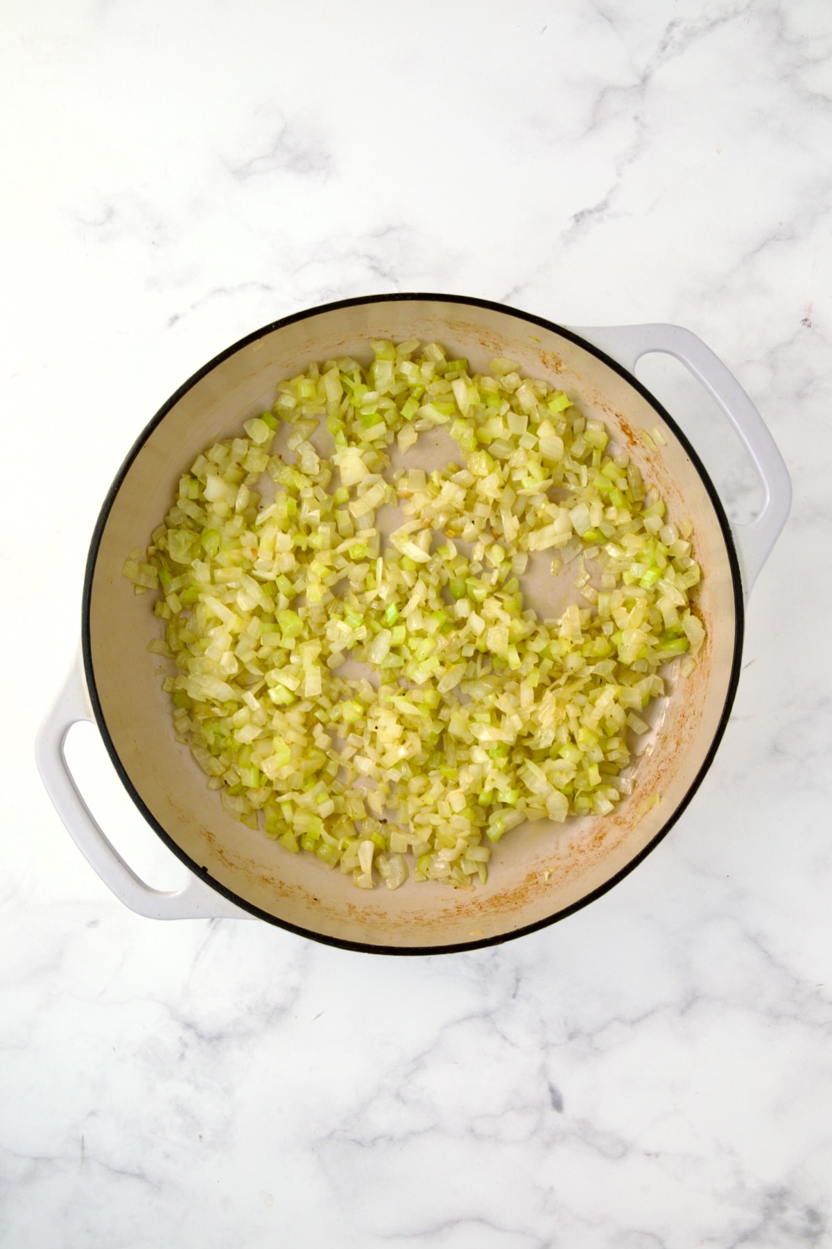 Cooked onions and celery in white enamel cast iron skillet.