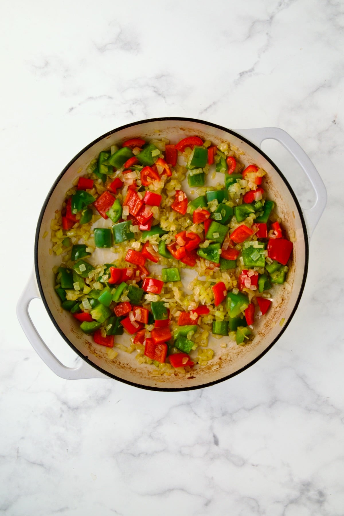 Cooked onions, celery and bell peppers in white enamel cast iron skillet.