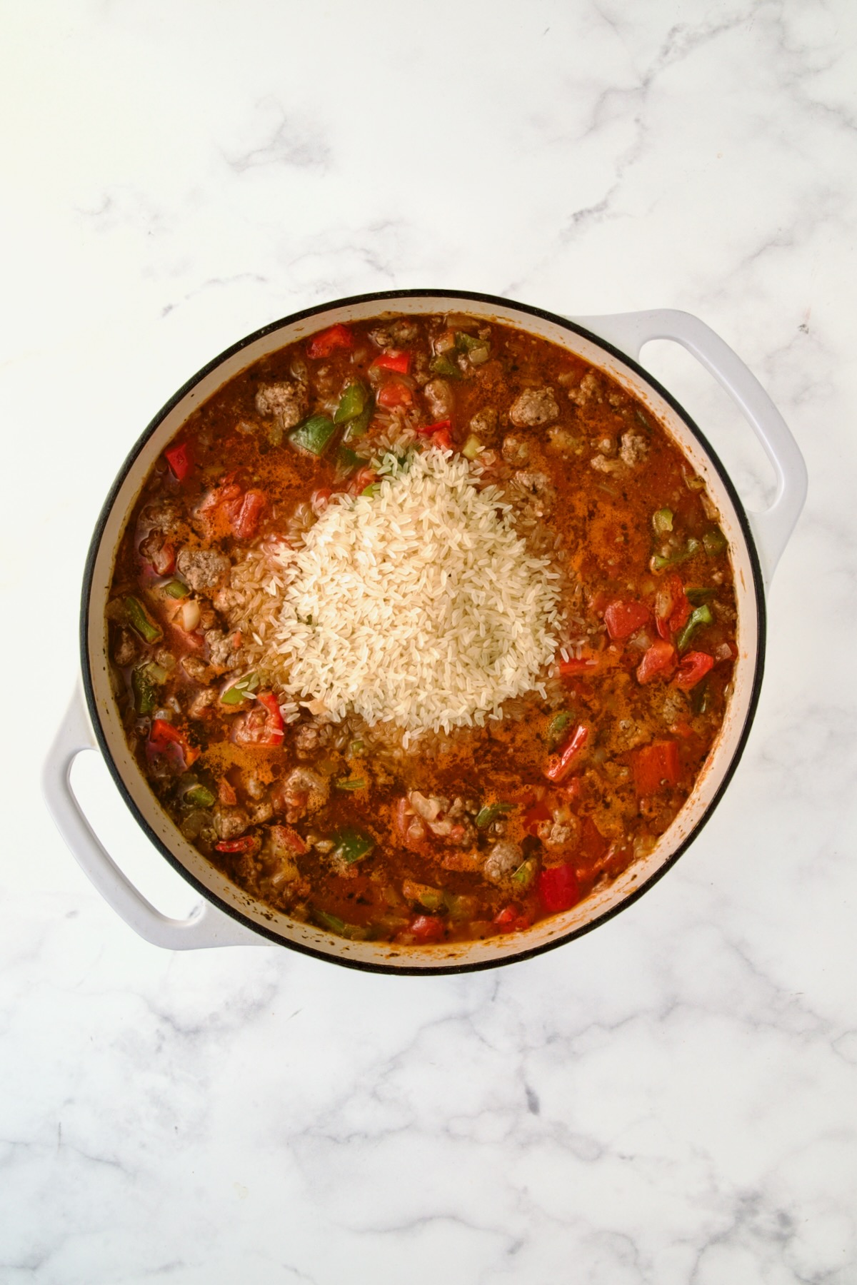 Rice added to ingredients in white enamel cast iron skillet.