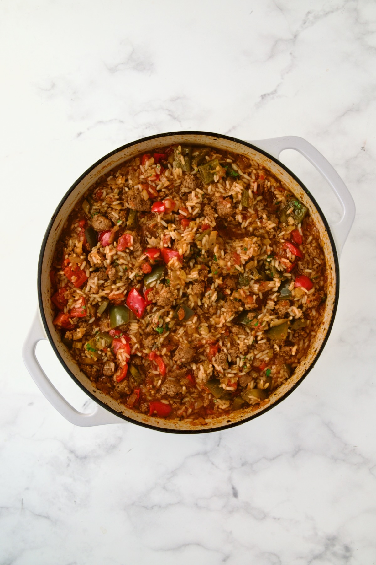 Cooked rice, beef, sauce and vegetables in white enamel cast iron skillet.