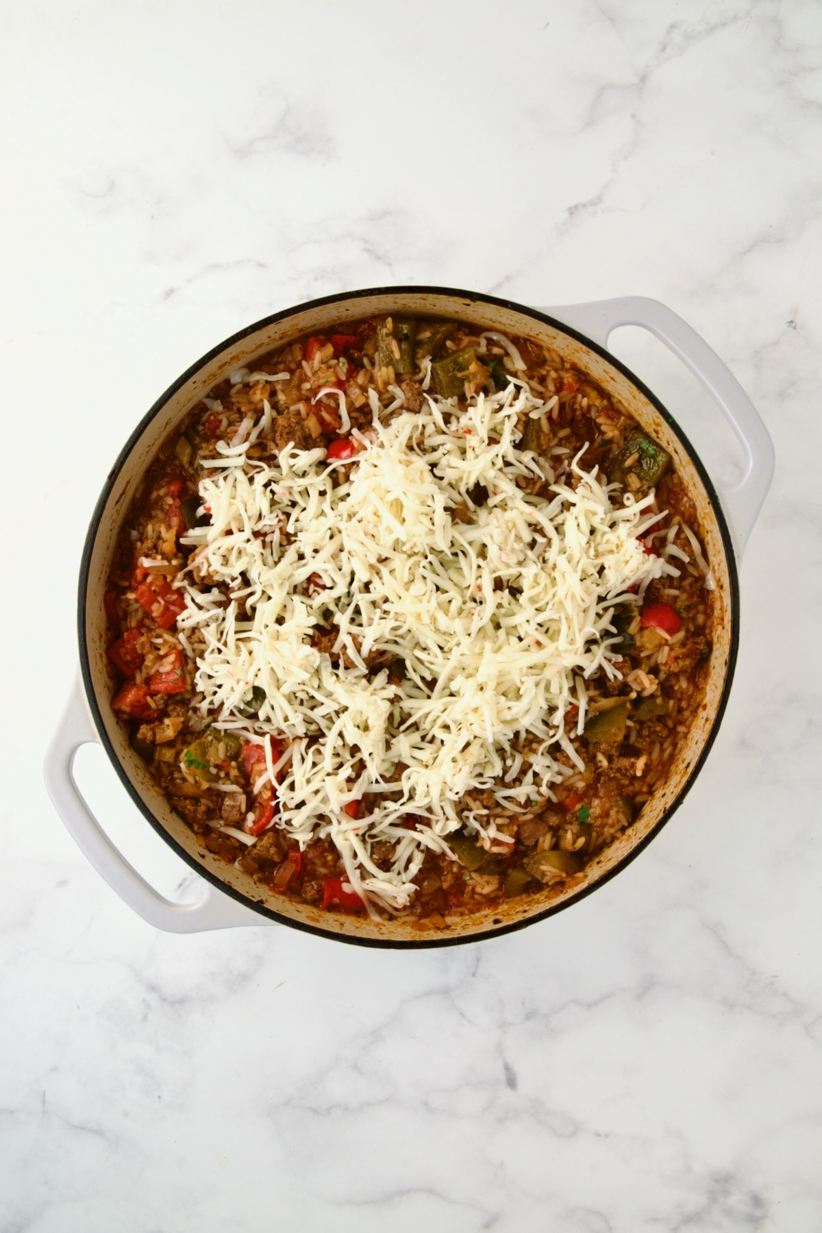 Cheese added to ingredients in white enamel cast iron skillet.