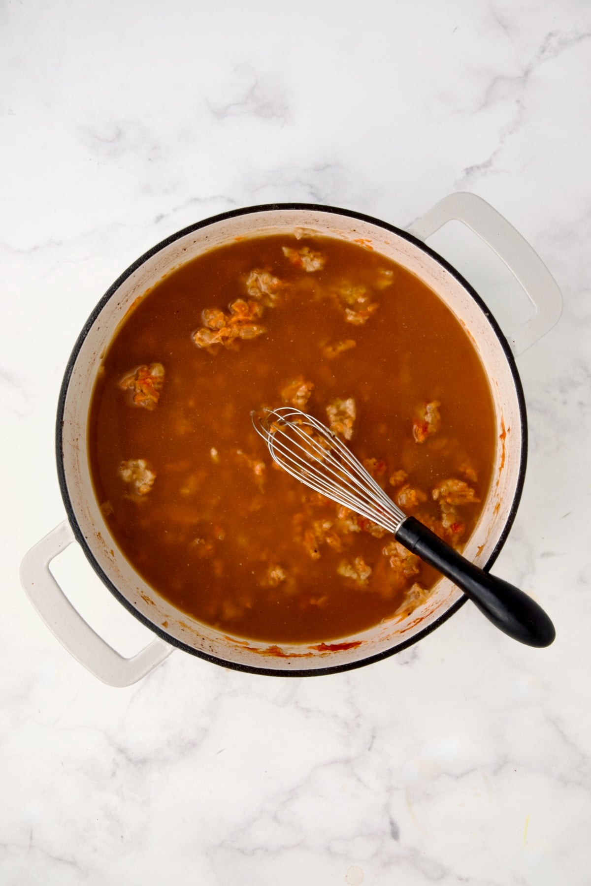 Broth added to tomato paste, wine, onions and flour smoothed out in white enamel cast iron skillet.