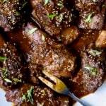 Korean Braised Beef Short Ribs on oval white platter with meat fork sprinkled with sesame seeds and thinly sliced scallions.