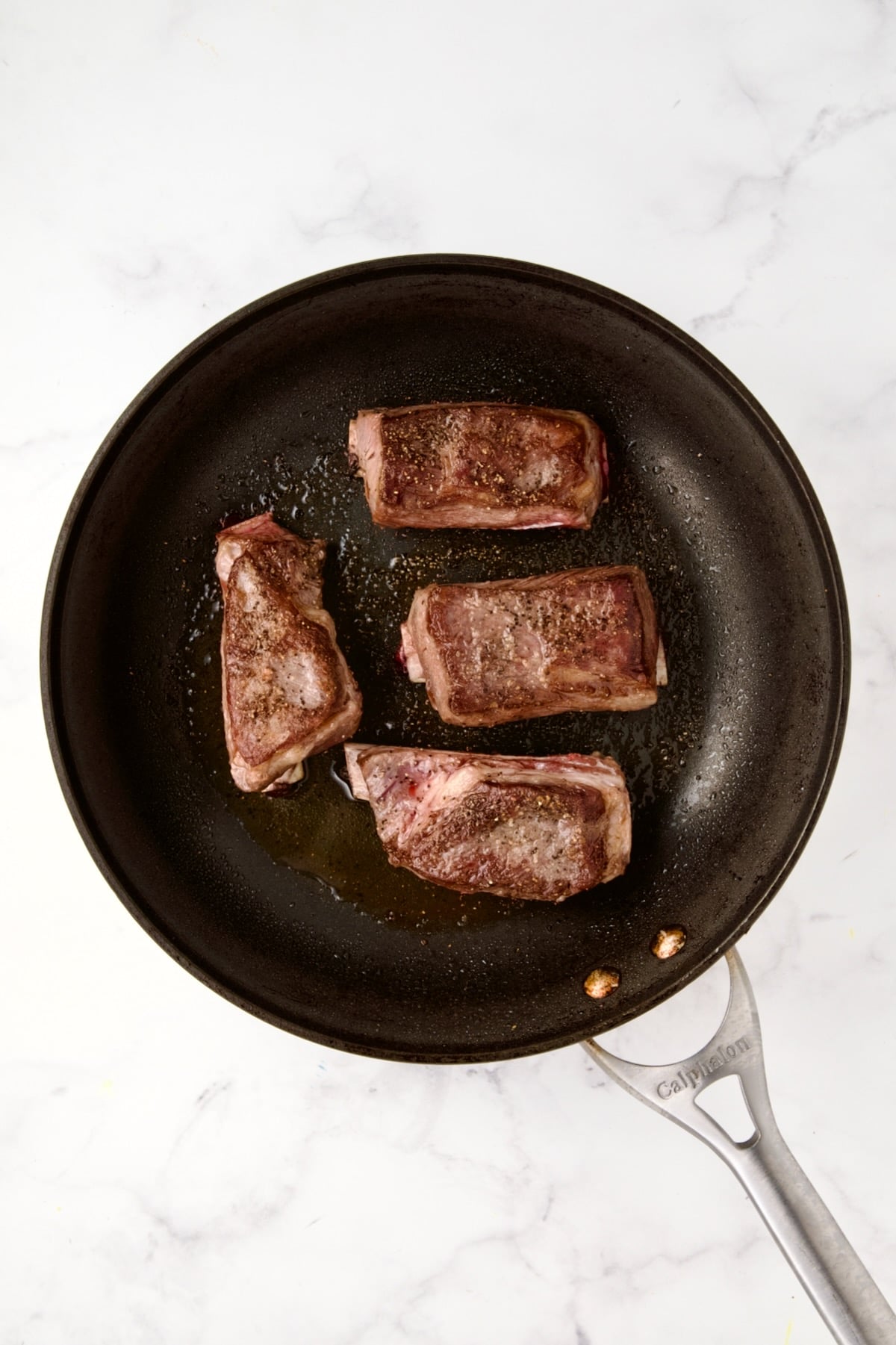 Four browned beef short ribs in nonstick skillet.