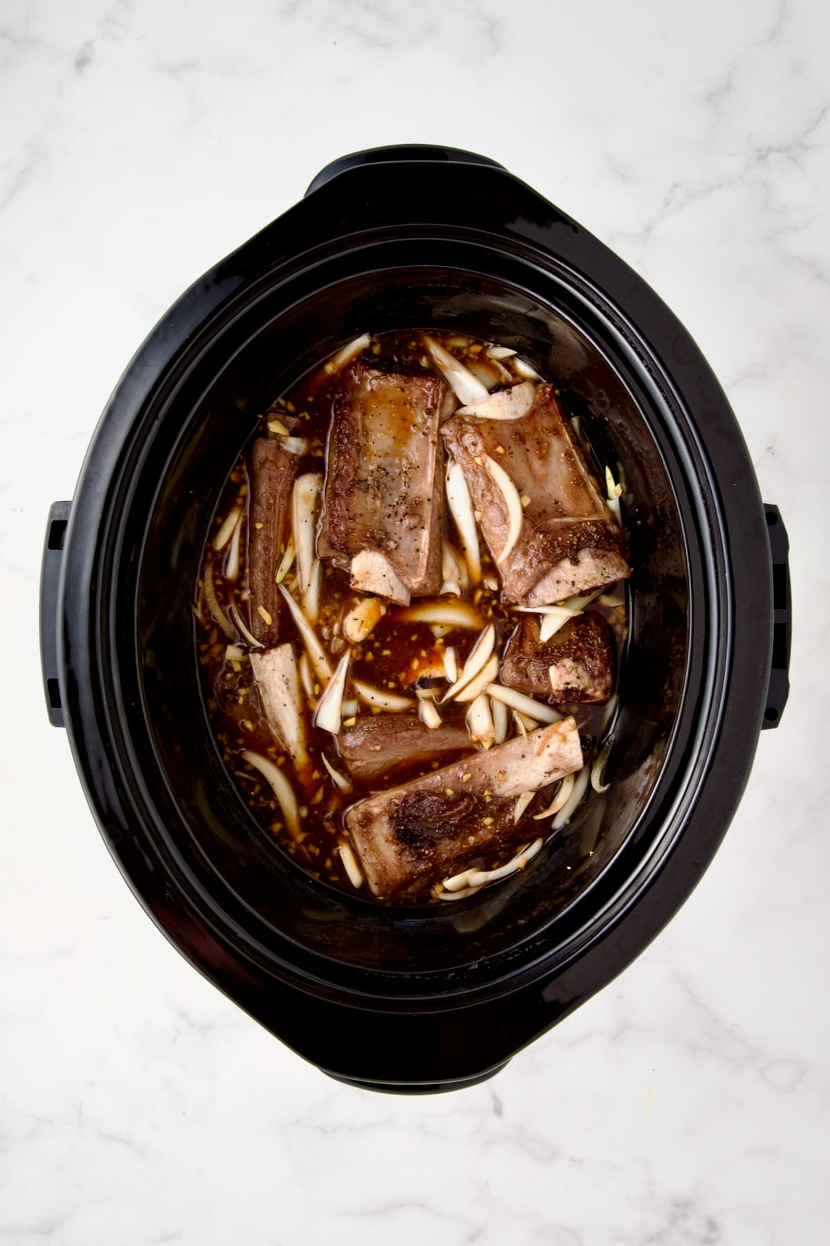 Ingredients for short ribs in slow cooker after ribs are placed inside.