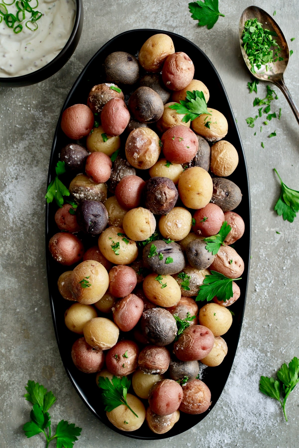 Salt Roasted Baby Potatoes on oval black patter with Sour Cream Horseradish Dip in a black bowl garnished with fresh parsley.