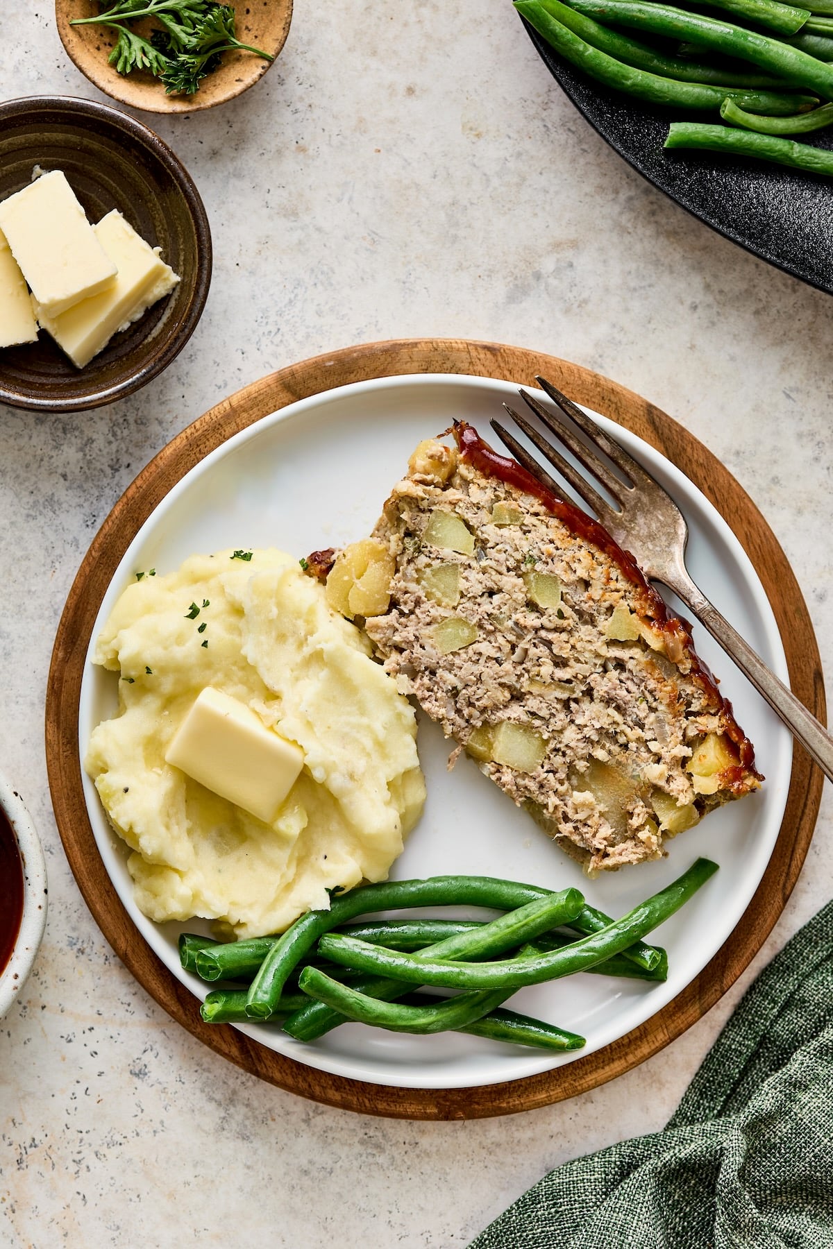 Slice of meatloaf, mashed potatoes and green beans on white plate with dinner fork.