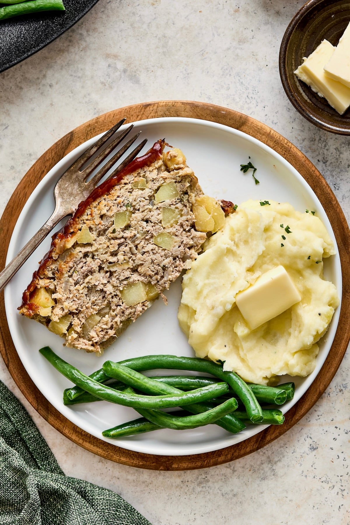 Slice of meatloaf, mashed potatoes and green beans on white plate with dinner fork.