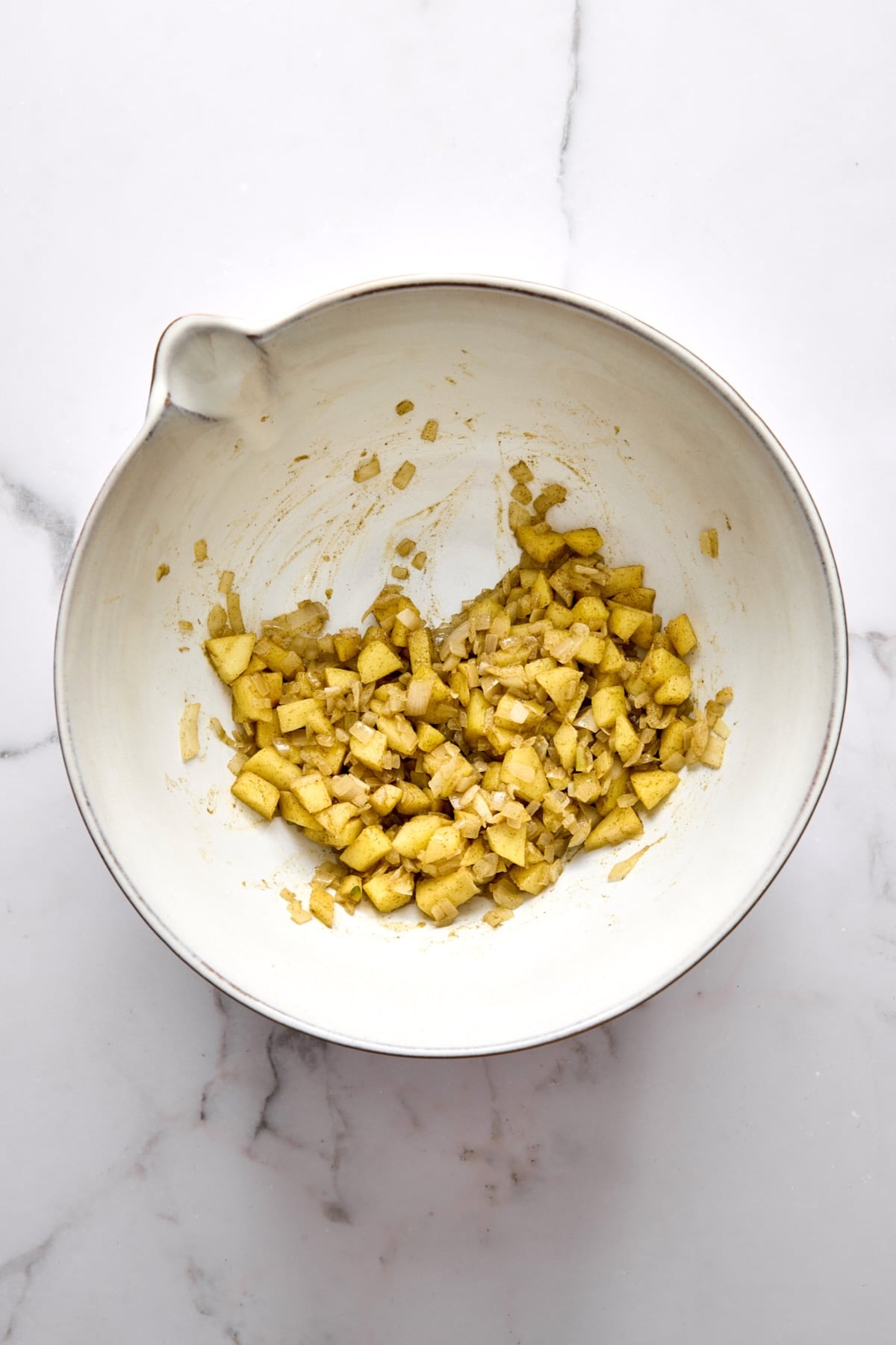 Cooked onions and apples in white mixing bowl.