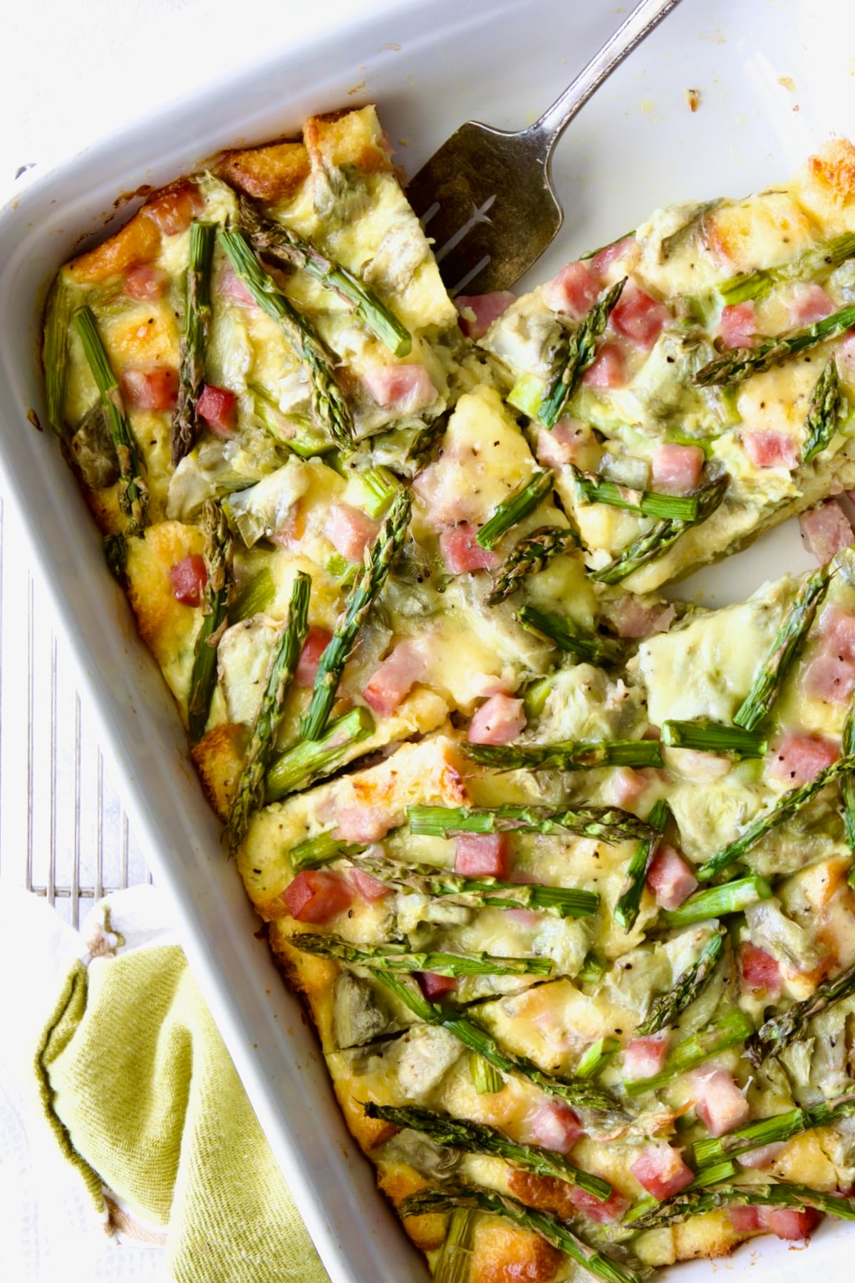 Brioche Breakfast Strata in white rectangular baking dish cut into pieces with one pieces.