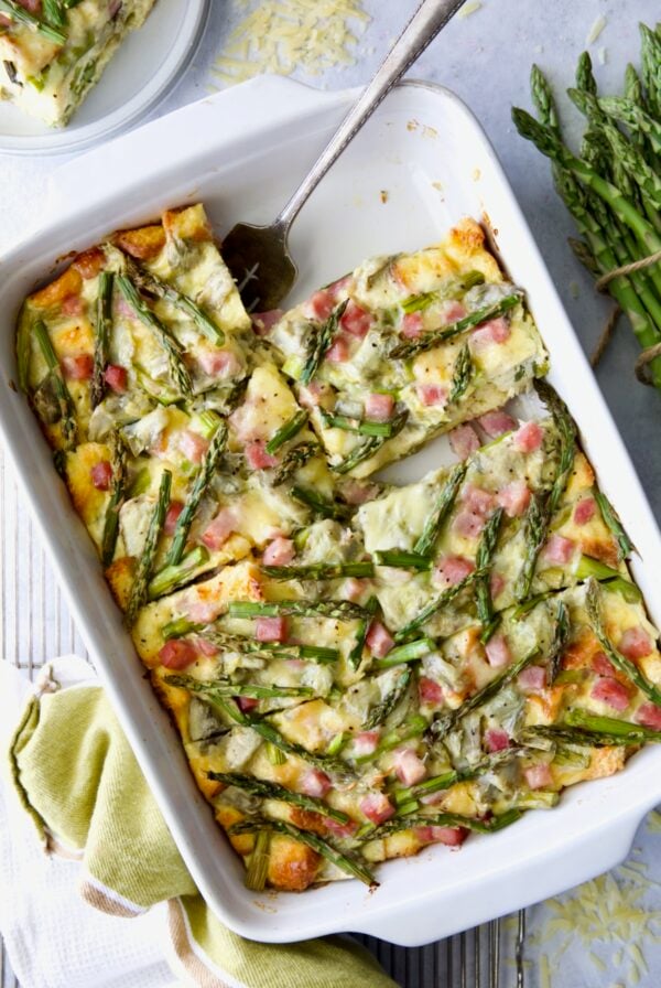 Brioche Breakfast Strata in white rectangular baking dish cut into pieces with one piece missing.