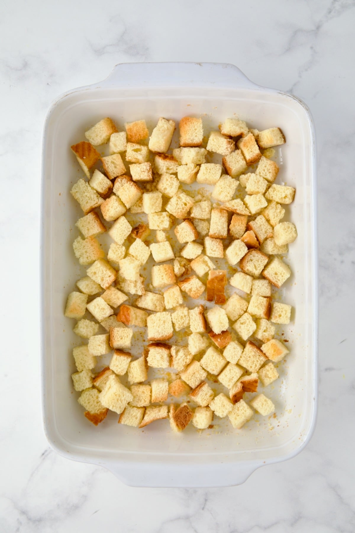 Half of the toasted brioche bread cubes in white rectangular baking dish.