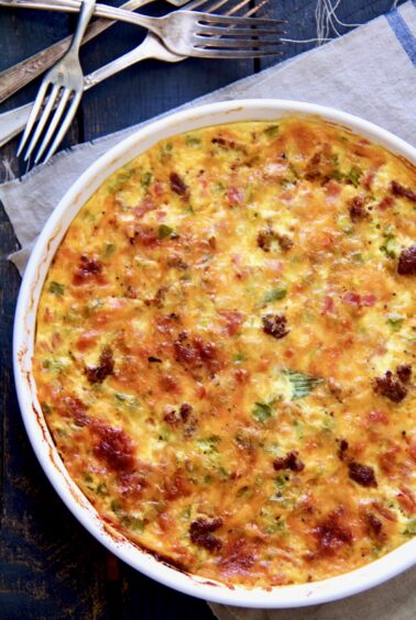 Uncut Crustless Quiche with Sausage Bacon and Ham in white quiche pan.