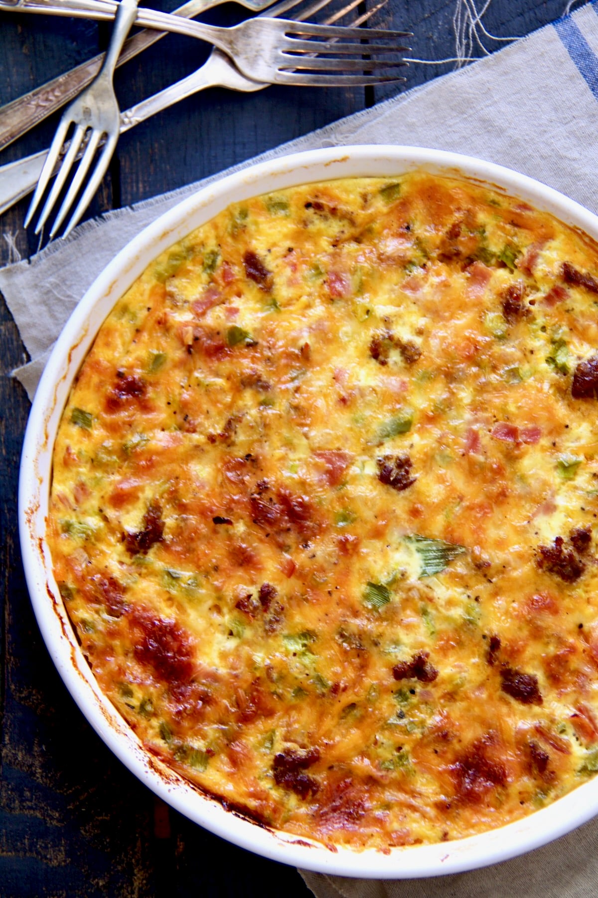 Uncut Crustless Quiche with Sausage Bacon and Ham in white quiche pan.