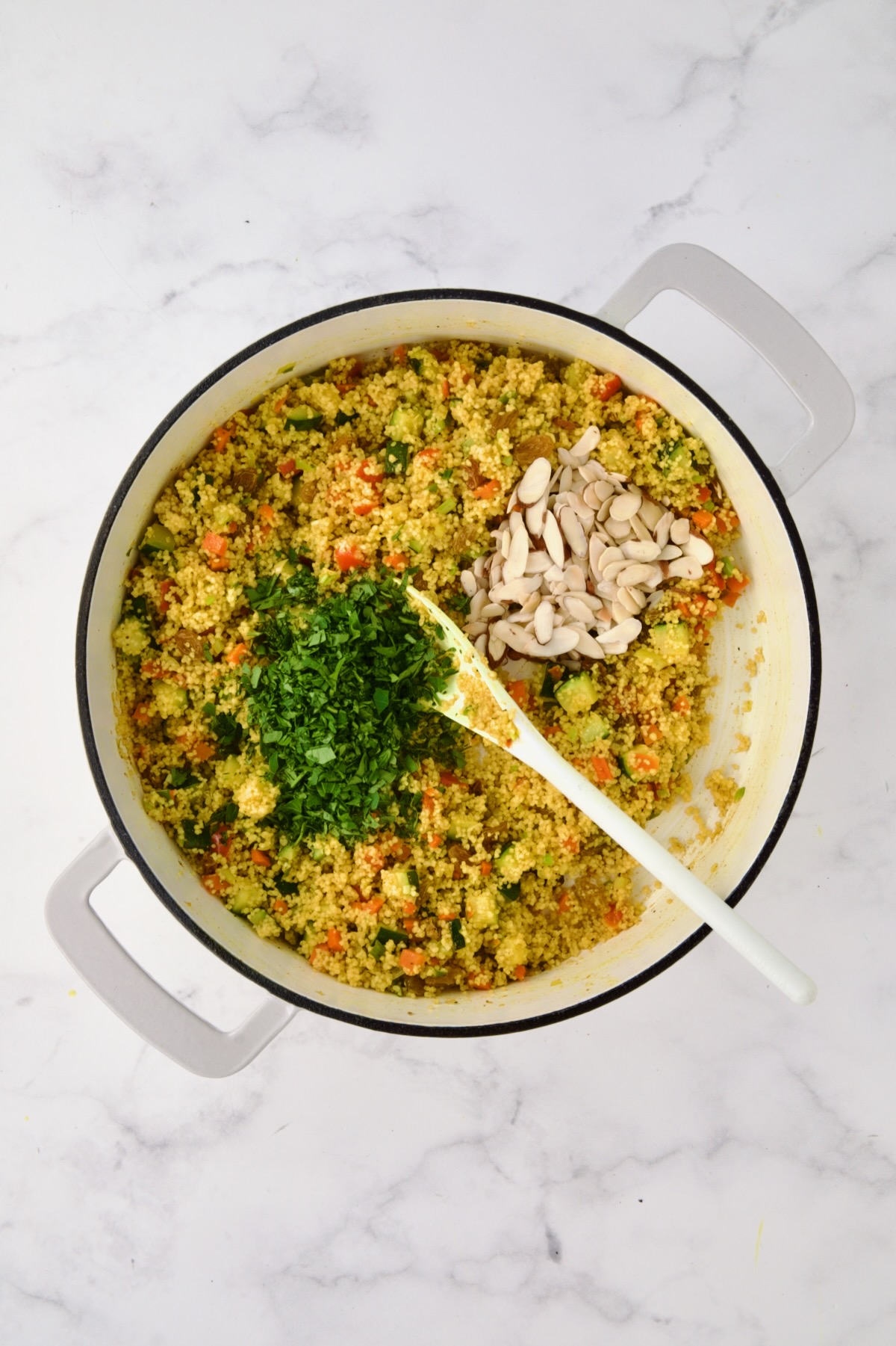 Chopped parsley and almonds added to cooked Jeweled Couscous in white enamel cast iron skillet.