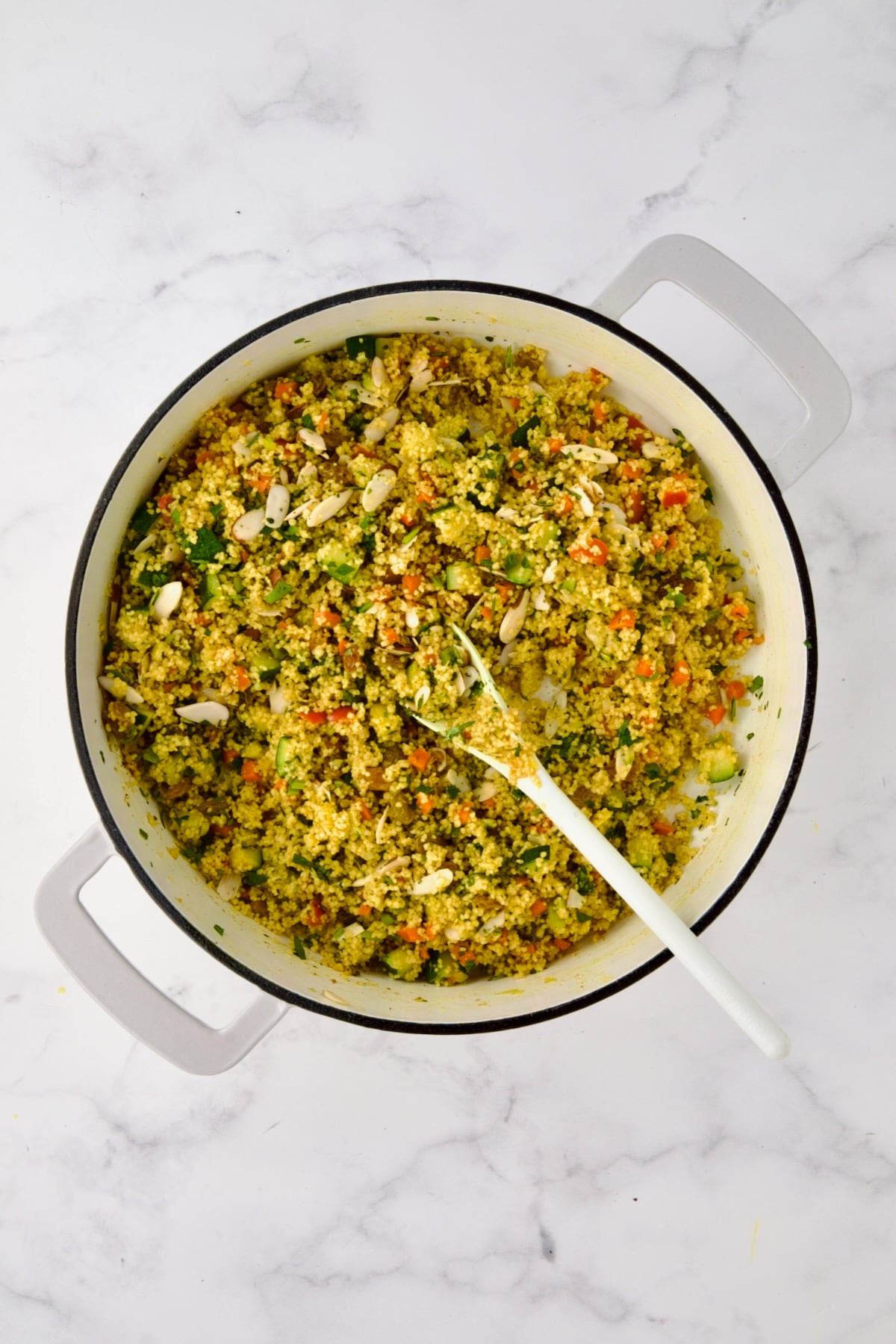 Jeweled Couscous in white enamel cast iron skillet with white mixing spoon.