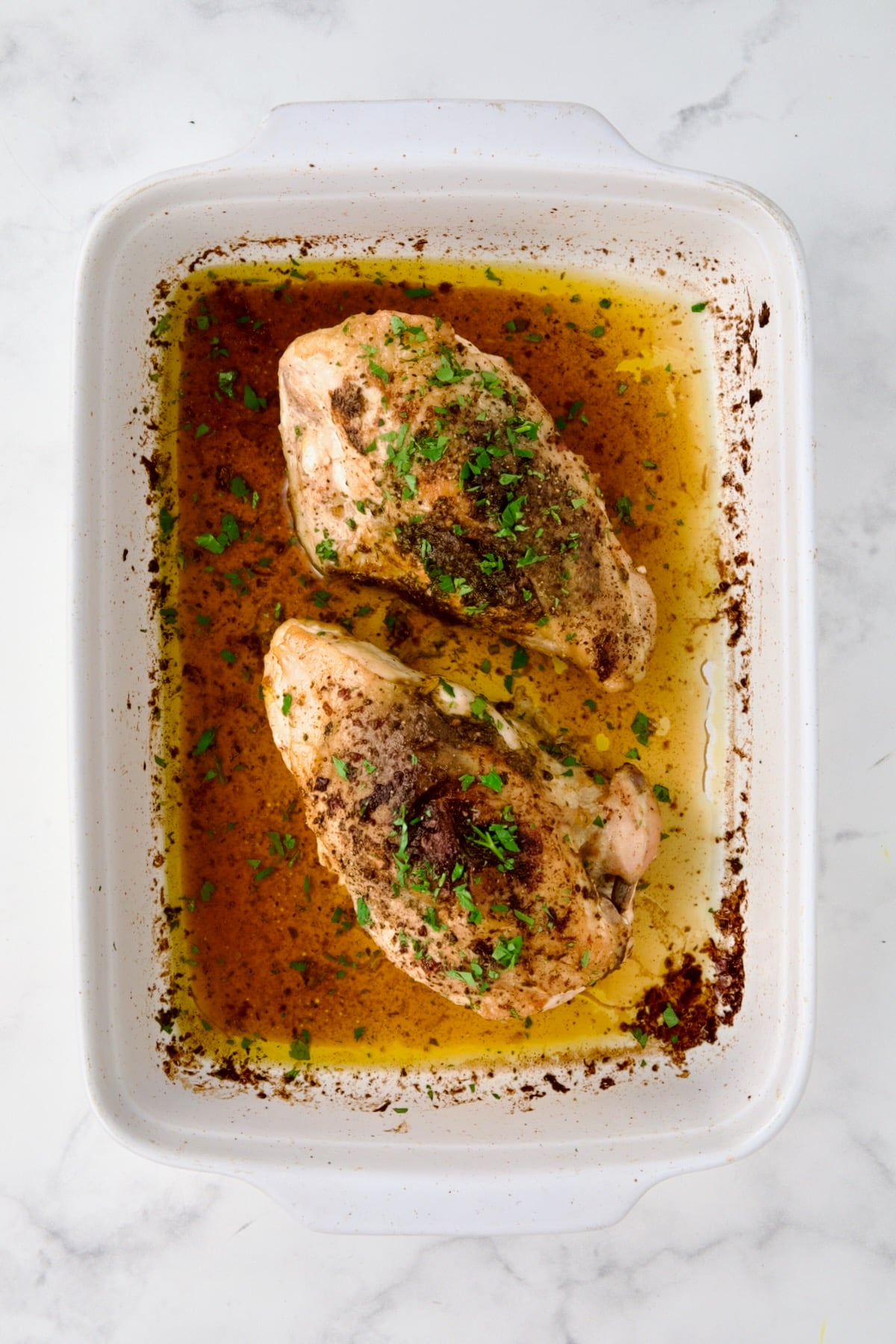 Two cooked Moroccan Chicken breasts in white rectangular baking dish.