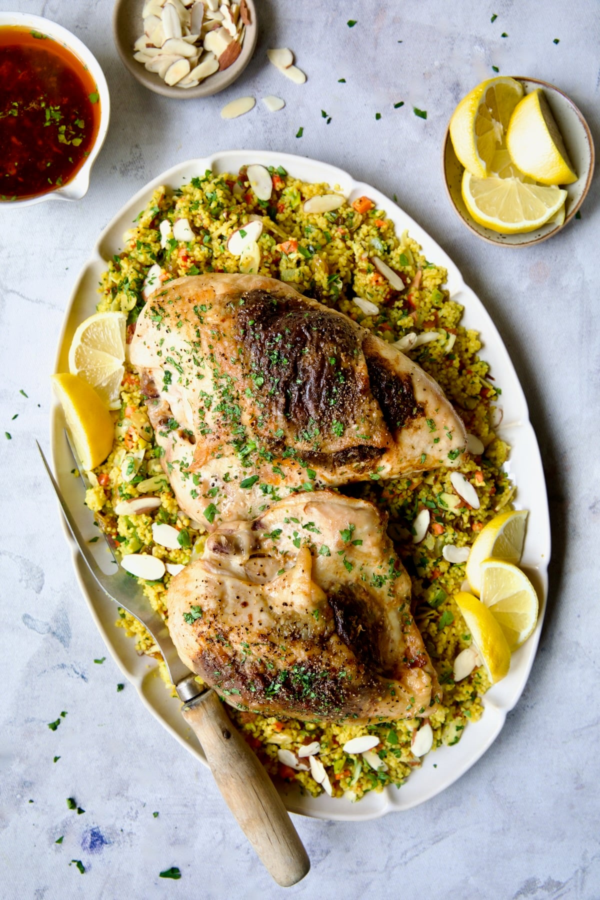 Two servings of Moroccan Chicken with Jeweled Couscous on oval white serving platter with meat fork.