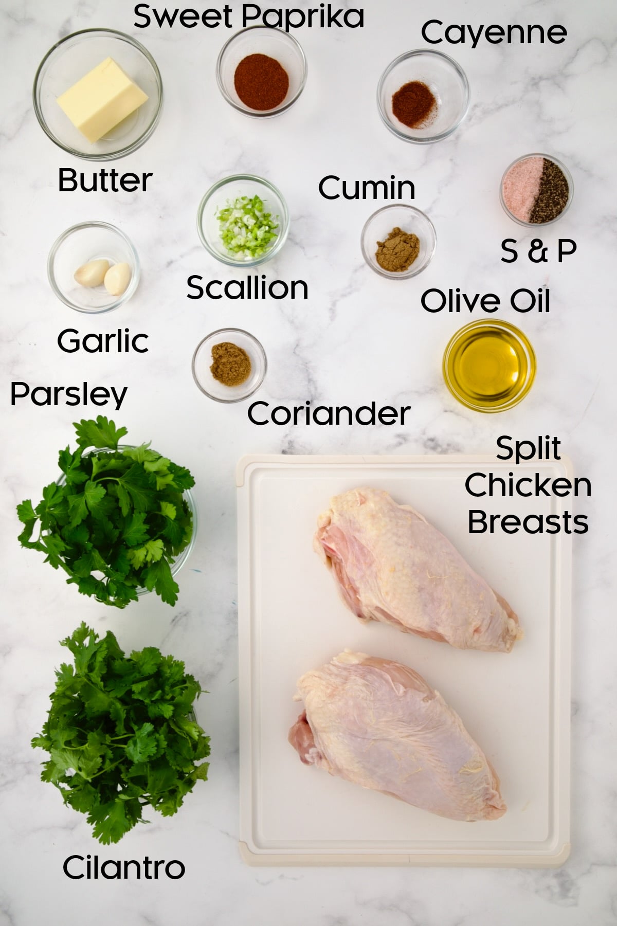 Ingredients for Moroccan Chicken in glass bowls with two split chicken breasts on a white plastic rectangular cutting board.