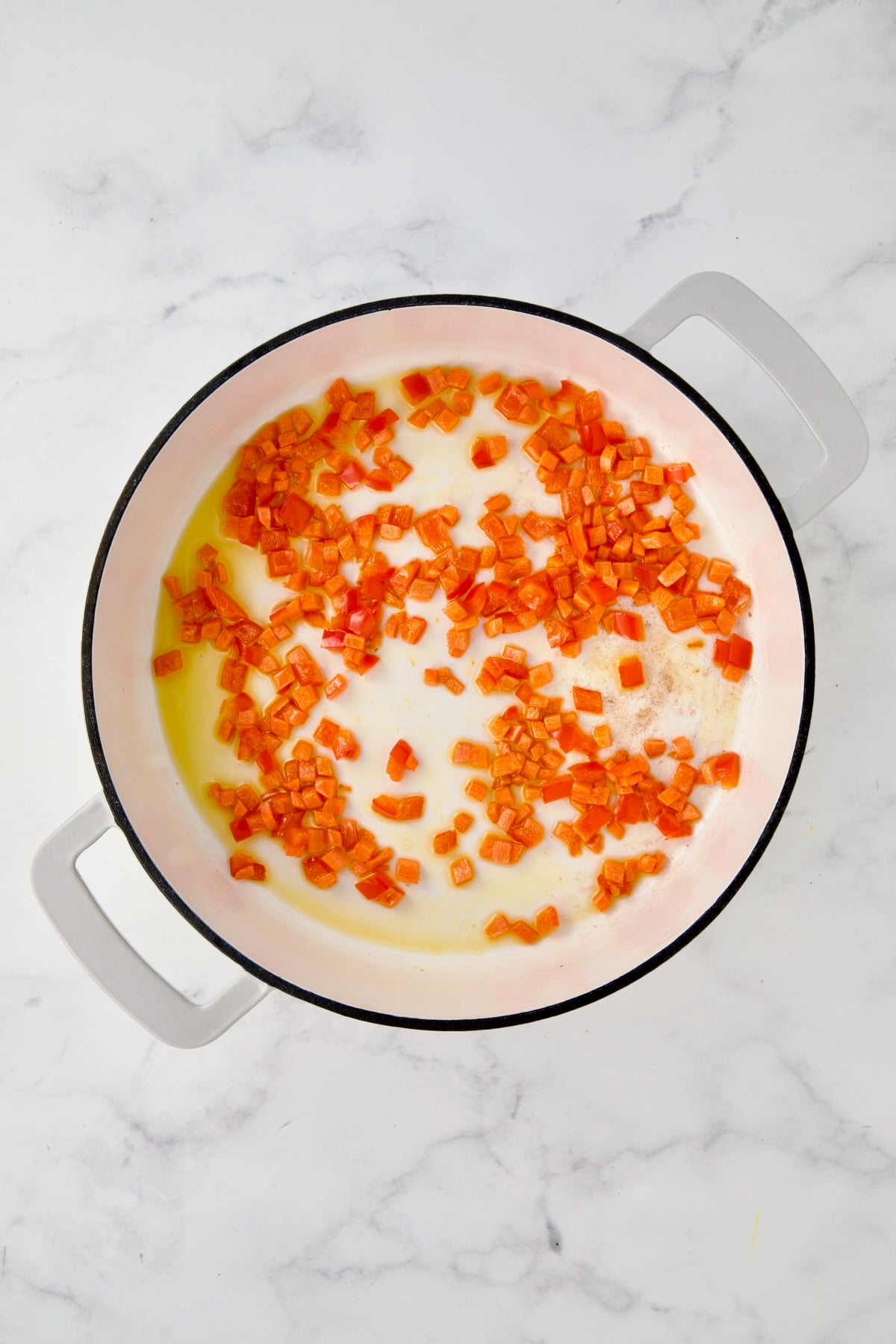 Cooked carrots and red bell pepper in white enamel cast iron skillet.