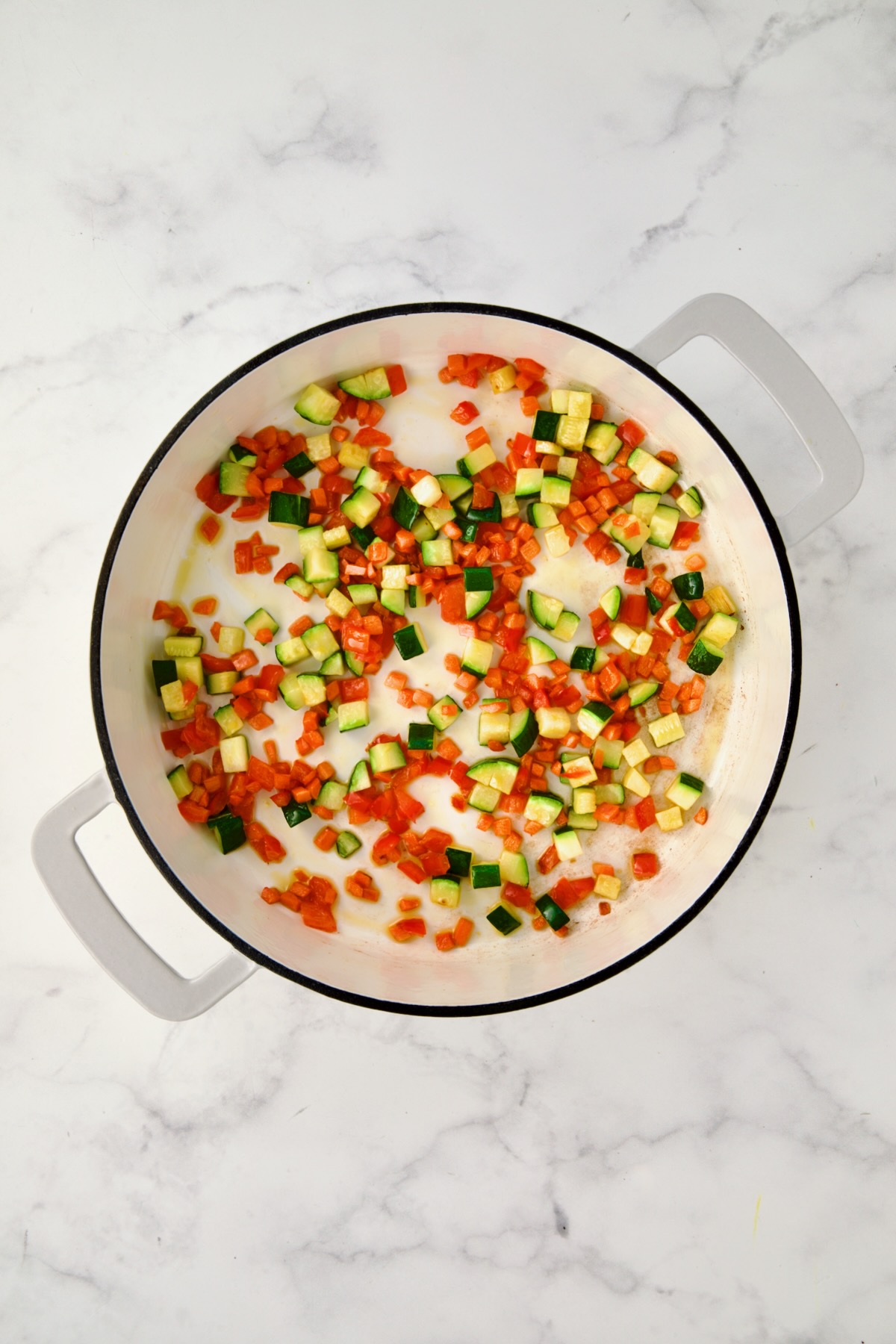 Cooked carrots, red bell pepper and zucchini in white enamel cast iron skillet.