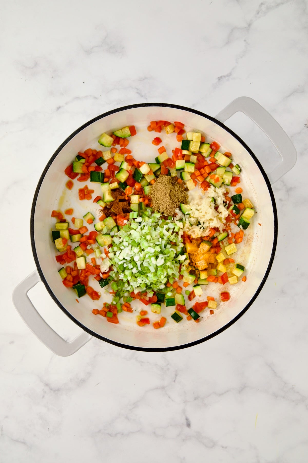 Cooked carrots, red bell pepper and zucchini in white enamel cast iron skillet with scallion and spices added.