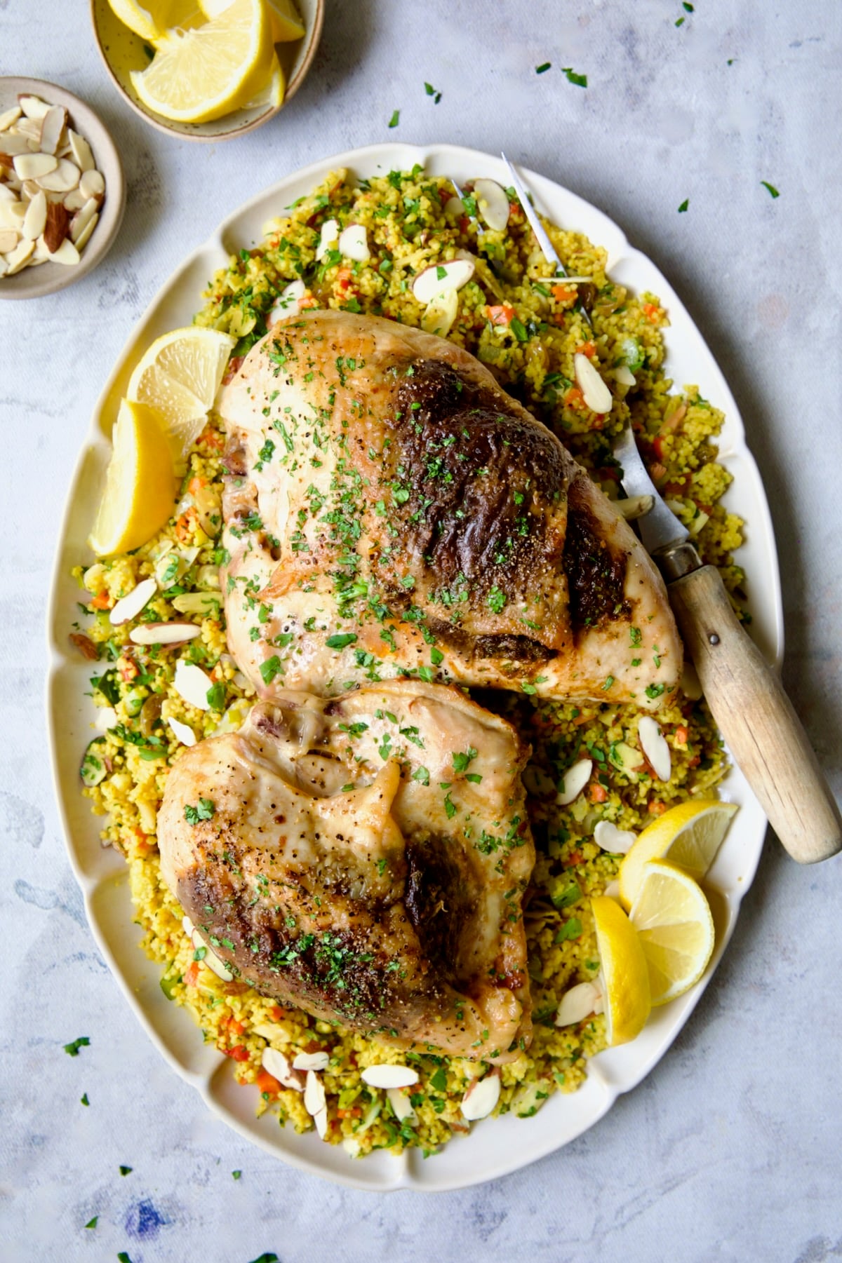 Two servings of Moroccan Chicken with Jeweled Couscous on oval white serving platter with meat fork.