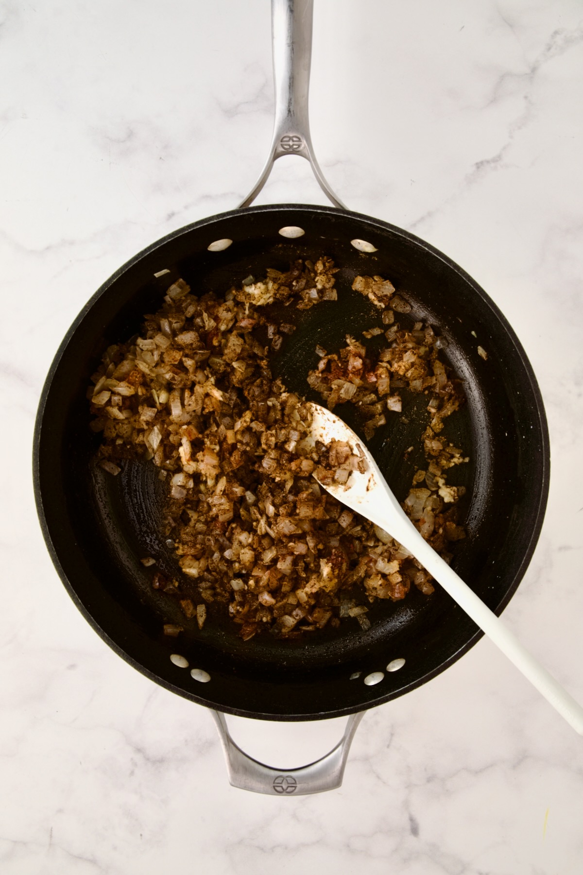 Spices being stirred into cooked onions.