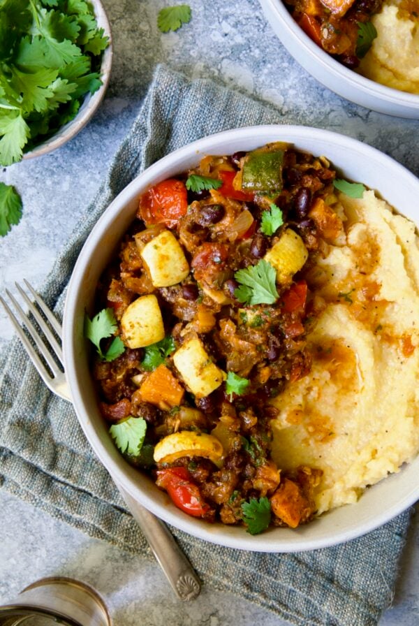 Roasted Vegetable Stew with Polenta in white bowl on blue napkin garnished with fresh cilantro leaves.