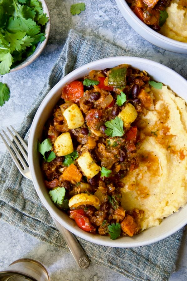 Roasted Vegetable Stew with Polenta in white bowl on blue napkin garnished with fresh cilantro leaves.