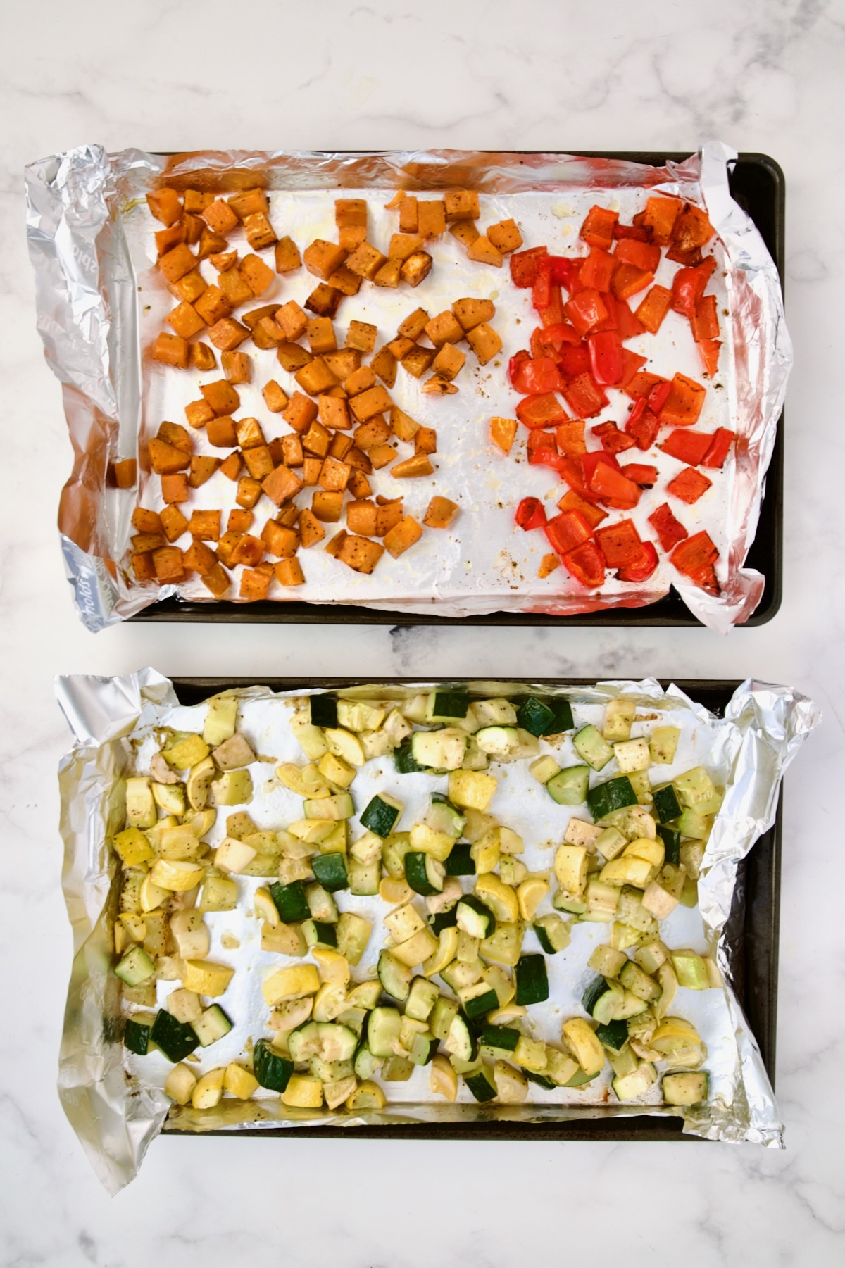Cubed sweet potato, red bell pepper, yellow squash and zucchini on aluminum foil-lined rimmed sheet pans after being roasted.